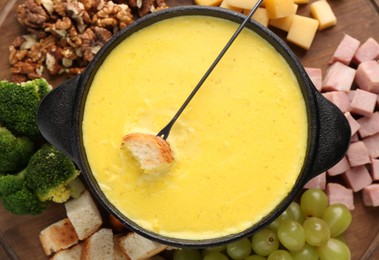 Fondue with tasty melted cheese, fork and different products on table, top view