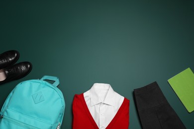 Stylish school uniform, backpack and notebook on green background, flat lay. Space for text