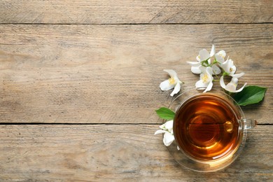 Photo of Glass cup of aromatic jasmine tea and fresh flowers on wooden table, flat lay. Space for text