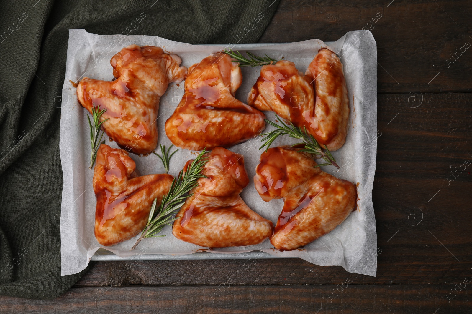 Photo of Raw marinated chicken wings and rosemary on wooden table, top view