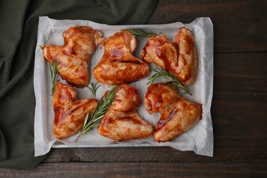 Photo of Raw marinated chicken wings and rosemary on wooden table, top view