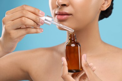 Photo of Woman with bottle of serum and dropper on light blue background, closeup