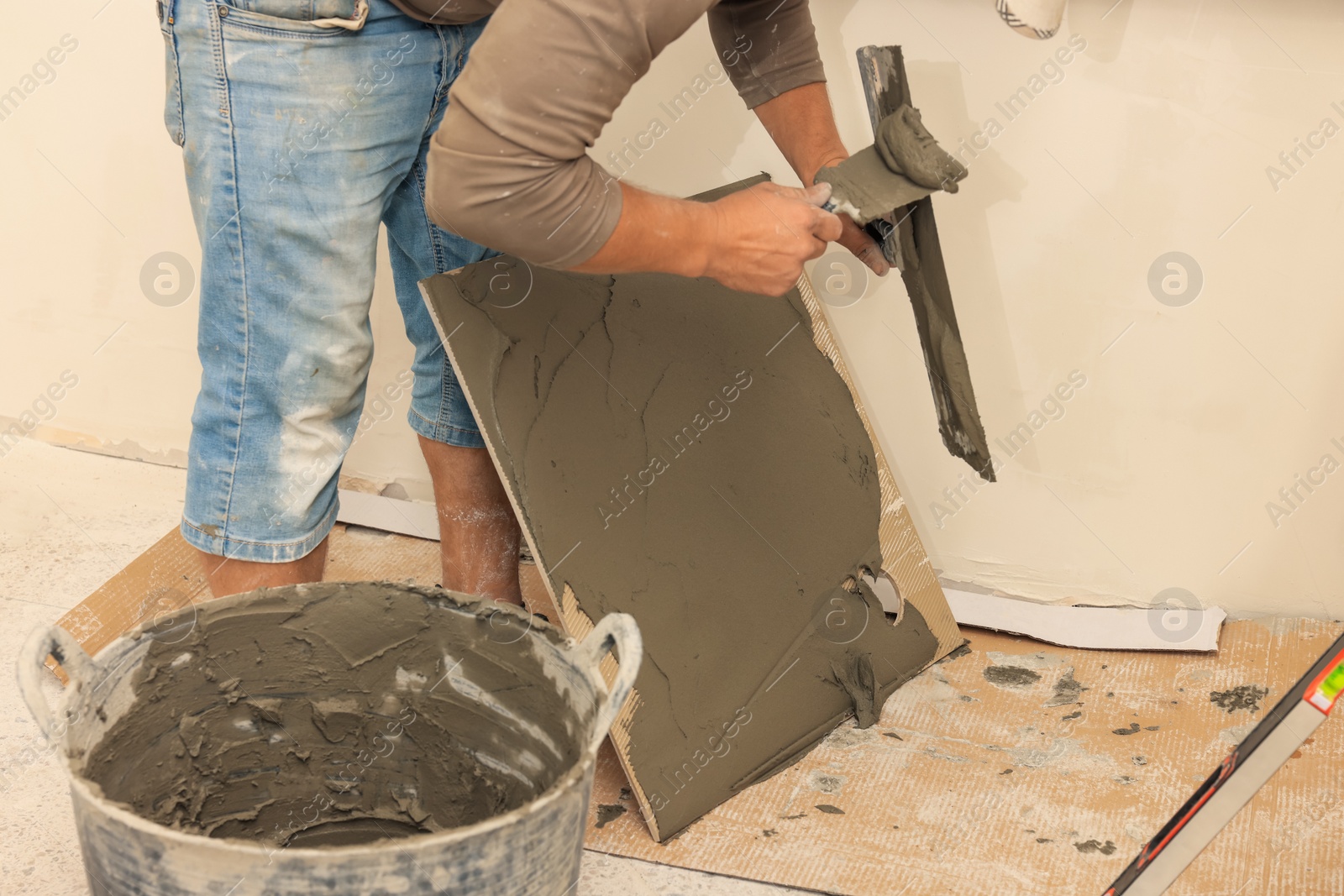 Photo of Worker spreading adhesive mix over tile with spatula, closeup