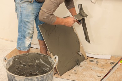 Worker spreading adhesive mix over tile with spatula, closeup