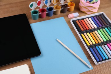 Photo of Blank sheet of paper, colorful chalk pastels, tablet and other drawing tools on wooden table. Modern artist's workplace
