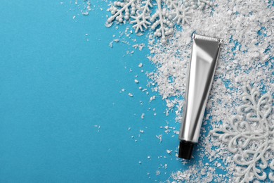 Photo of Tube of hand cream and decorative snow on light blue background, flat lay with space for text. Winter skin care