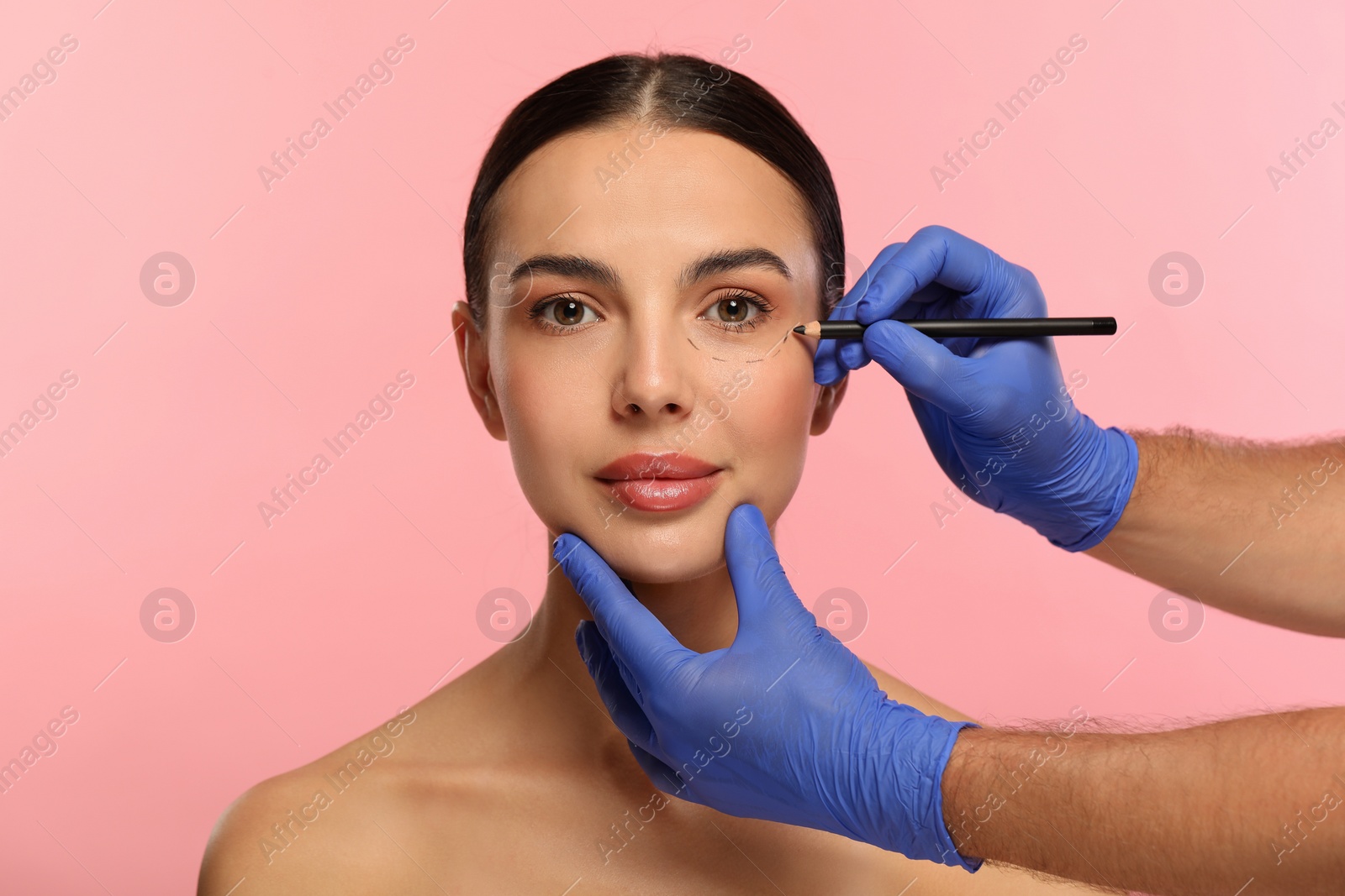 Photo of Doctor with pencil preparing patient for cosmetic surgery operation on pink background