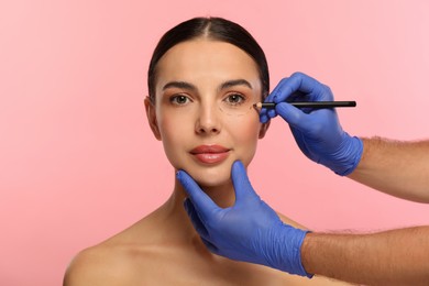 Doctor with pencil preparing patient for cosmetic surgery operation on pink background