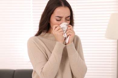 Sick woman with tissue sneezing at home. Cold symptoms