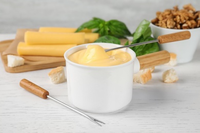 Photo of Pot of tasty cheese fondue and products on white wooden table