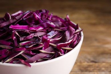 Photo of Fresh chopped red cabbage in bowl on wooden table, closeup
