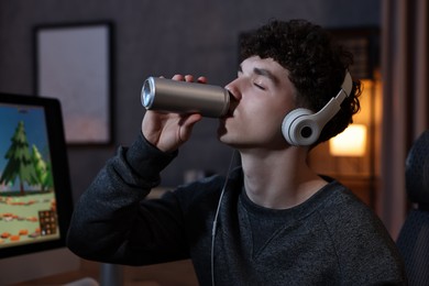 Young man with energy drink and headphones playing video game at home