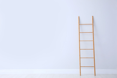 Modern wooden ladder near white wall. Space for text