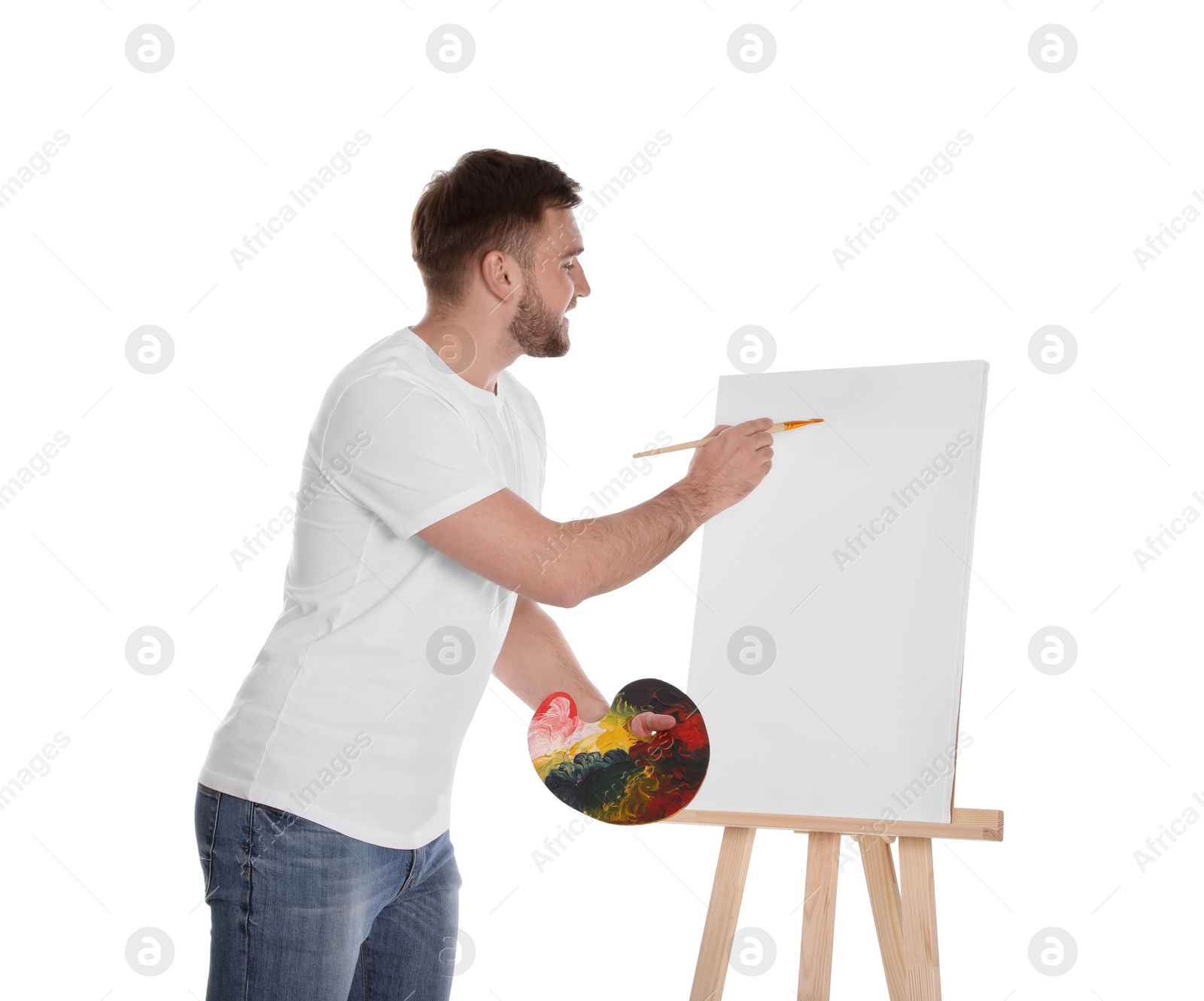 Photo of Man painting with brush on easel against white background. Young artist