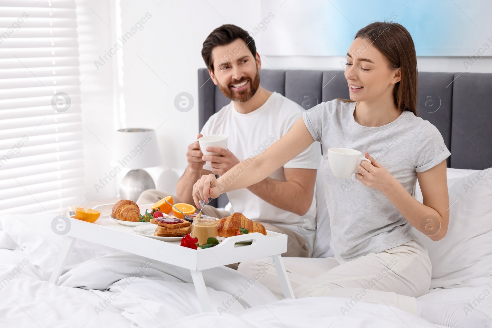 Photo of Happy couple eating tasty breakfast on bed at home