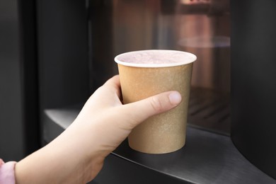 Girl holding paper cup with hot drink near coffee vending machine, closeup