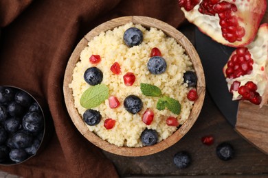Photo of Bowl of tasty couscous with blueberries, pomegranate and mint on table, flat lay