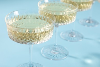 Photo of Glasses of expensive white wine on light blue background, closeup