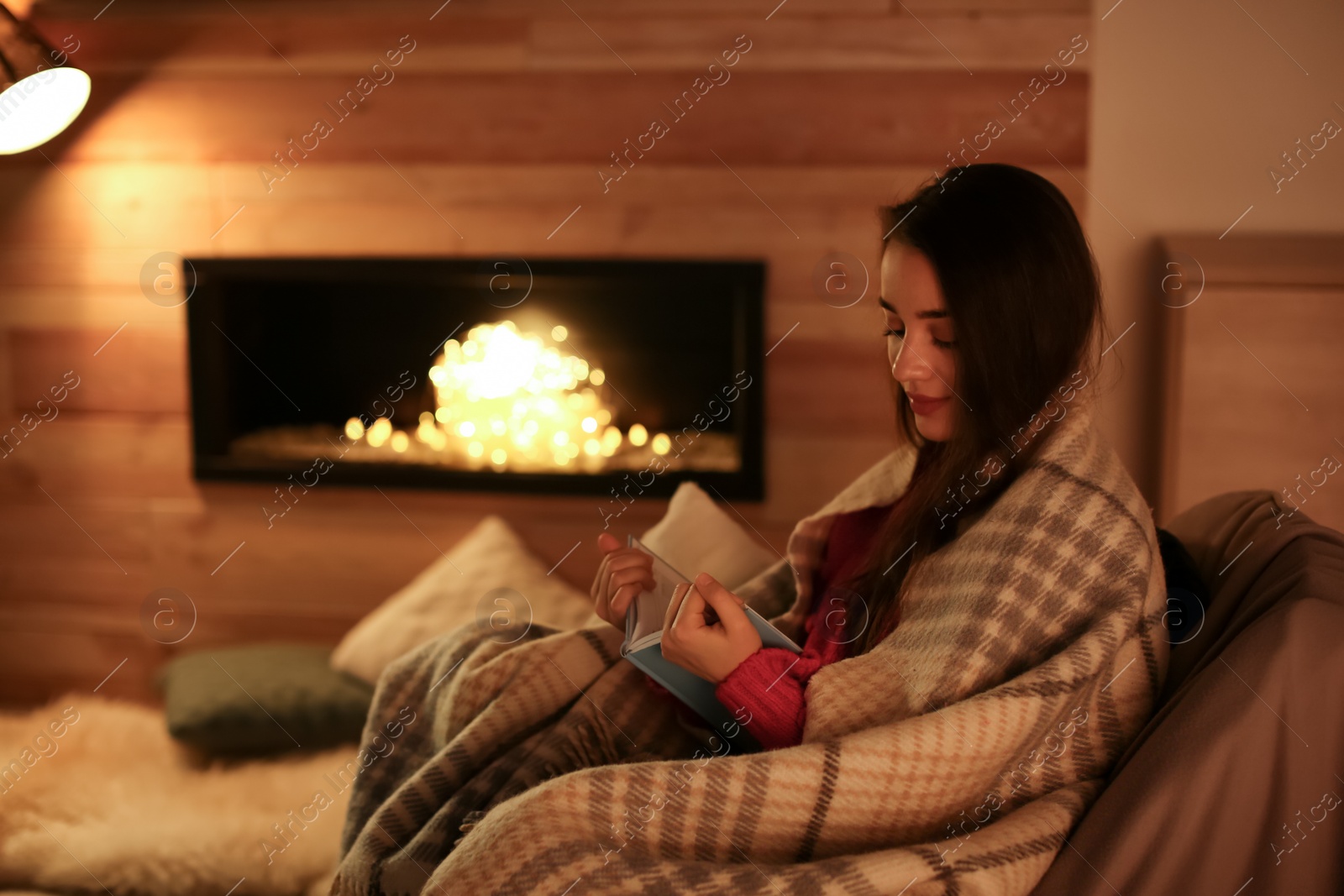 Photo of Woman reading book near decorative fireplace at home. Winter season