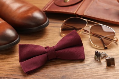 Stylish burgundy bow tie, sunglasses, shoes, brown wallet and cufflinks on wooden background