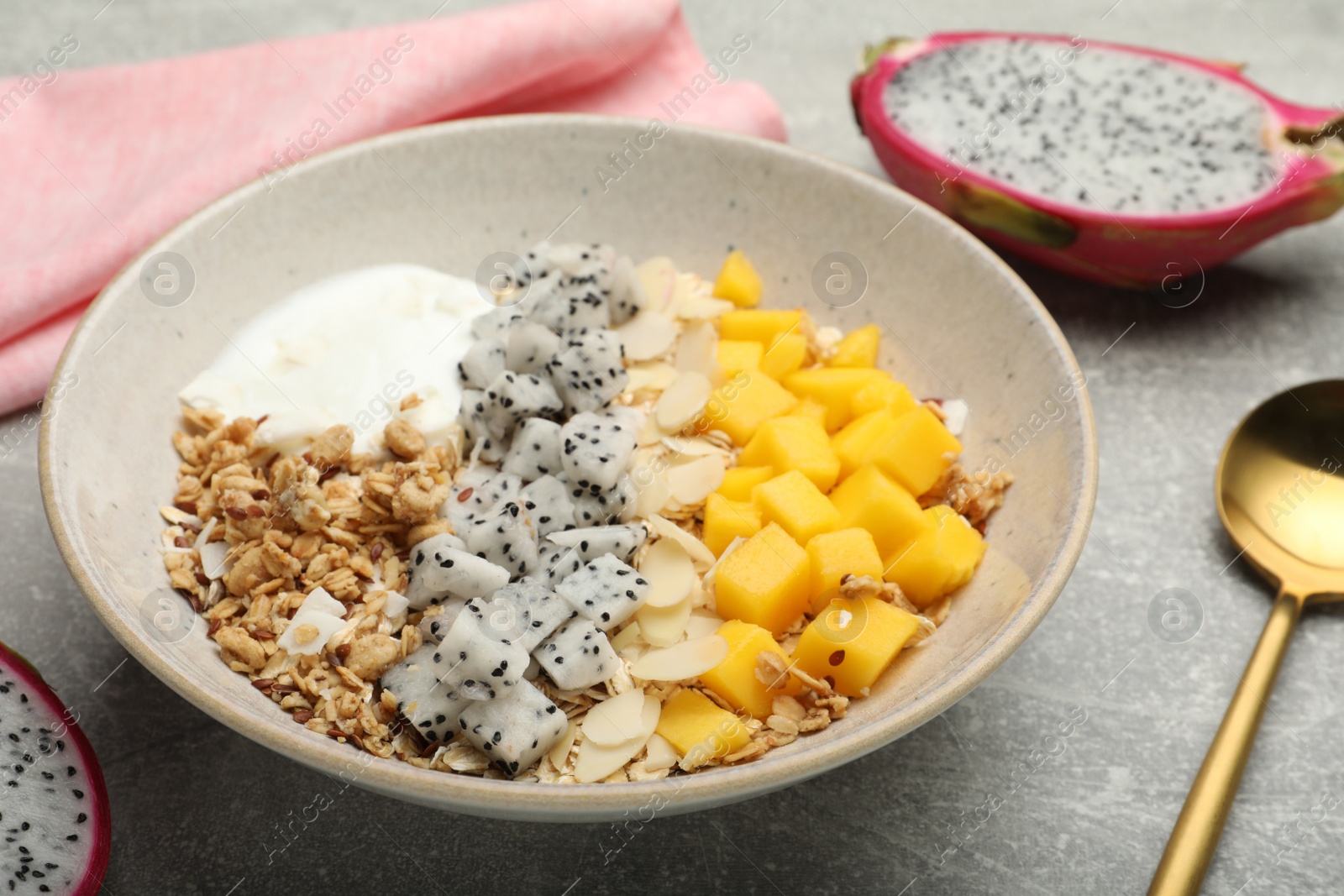 Photo of Bowl of granola with pitahaya, mango and yogurt on light grey table