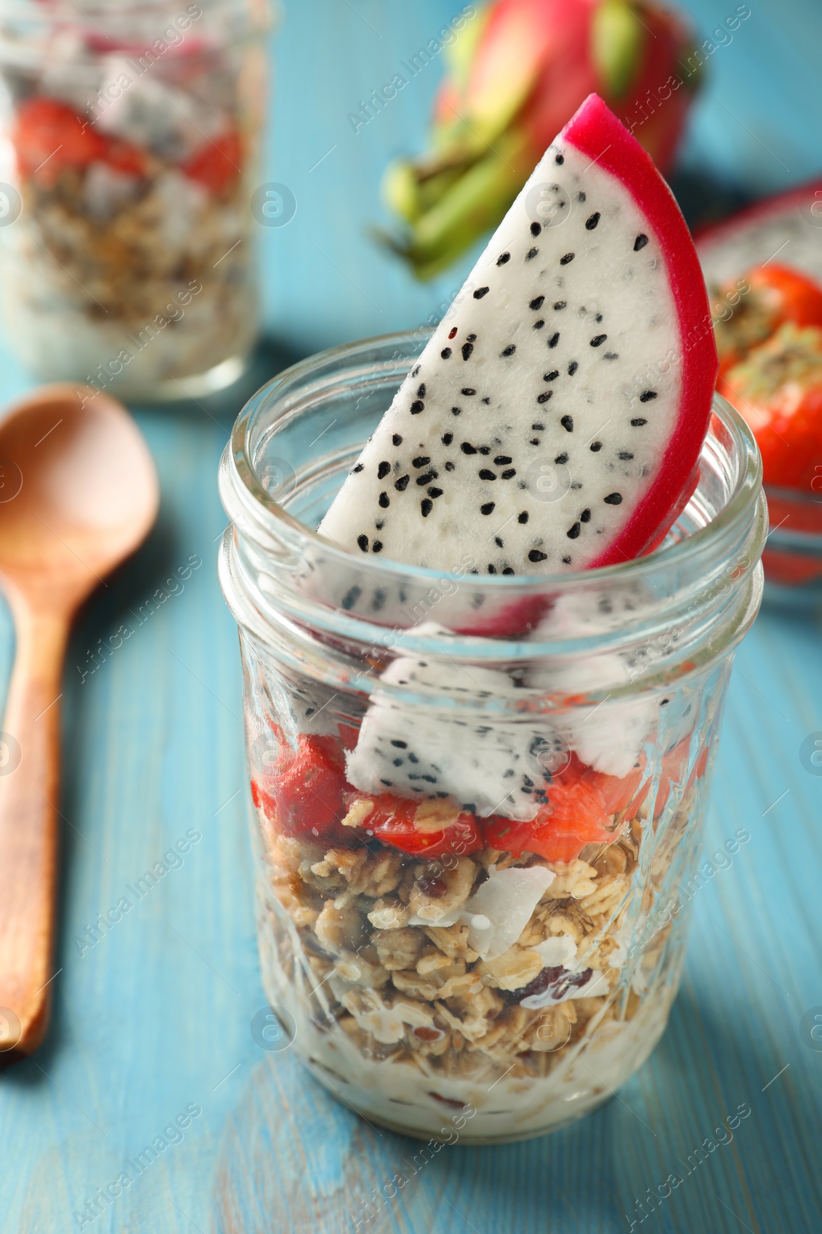 Photo of Granola with strawberries and pitahaya in glass jar on light blue wooden table