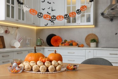 Photo of Kitchen decorated for Halloween. Pumpkins, candies and bunch of garlic on wooden table