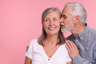 Photo of Senior man kissing his beloved woman on pink background, space for text