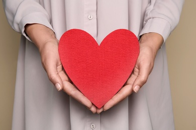 Young woman holding red heart on color background, closeup