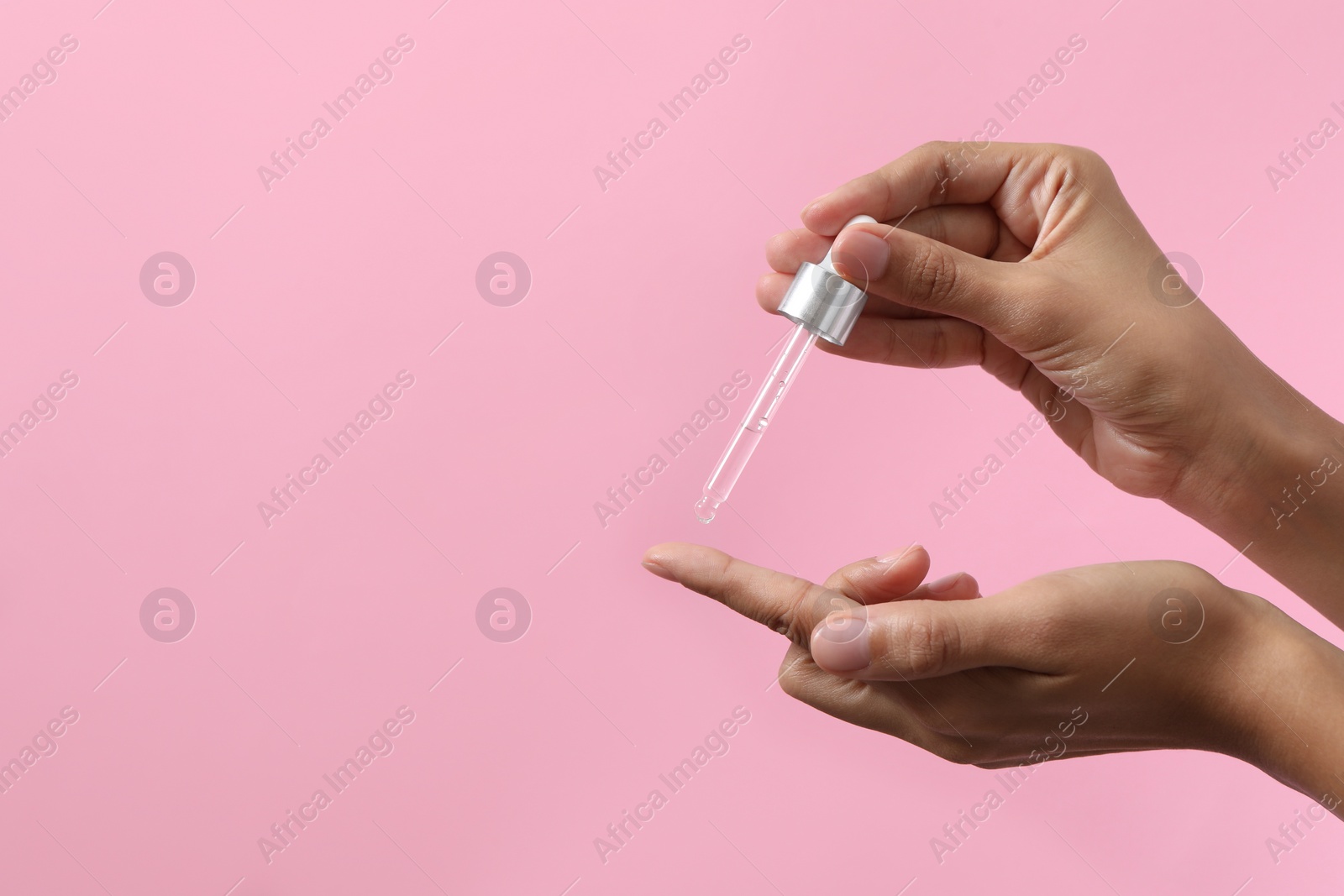 Photo of Woman applying cosmetic serum onto her finger on pink background, closeup. Space for text