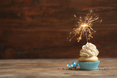 Birthday cupcake with sparkler on wooden table. Space for text