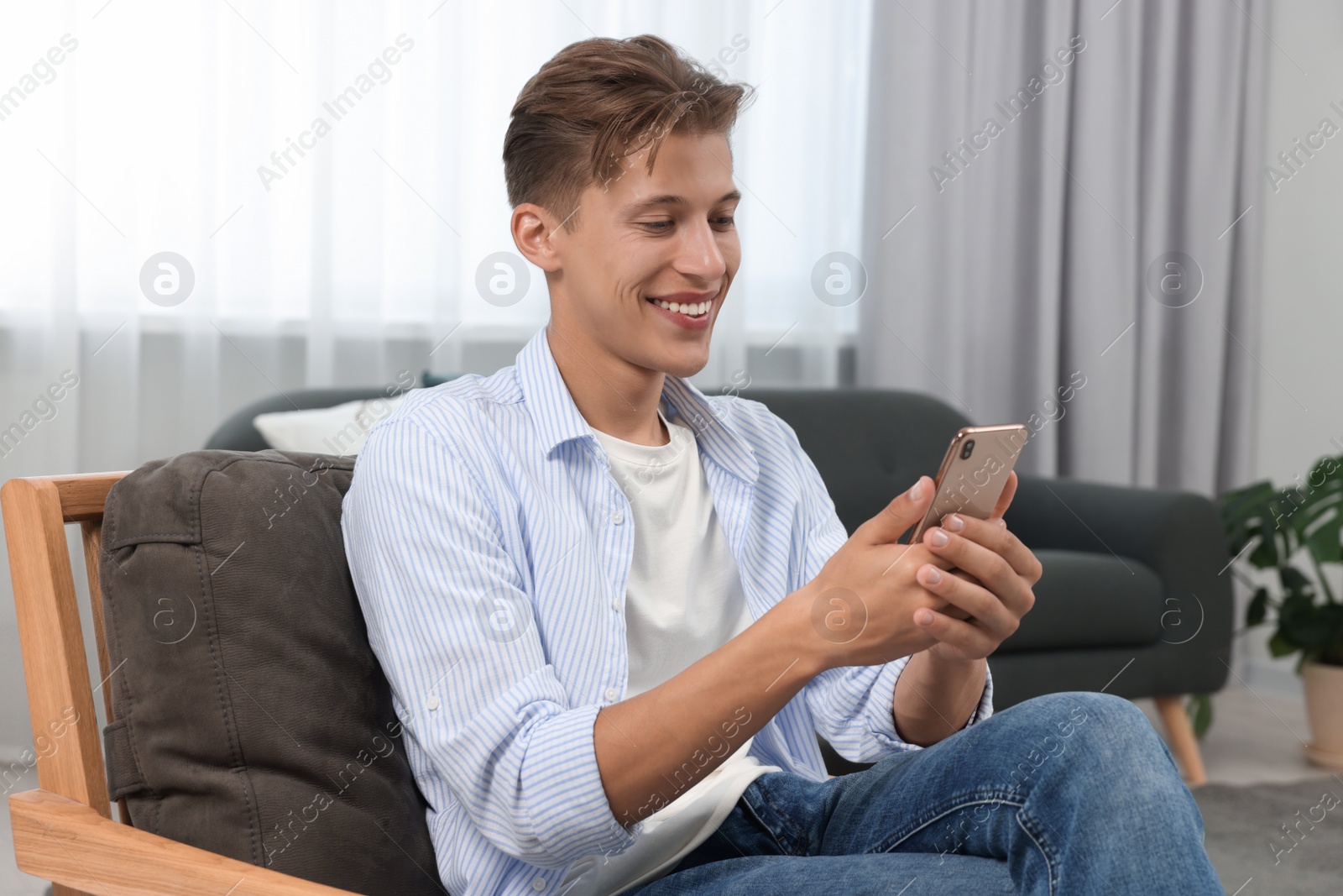 Photo of Happy young man having video chat via smartphone on armchair indoors