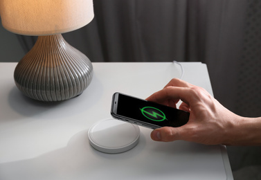 Man putting smartphone on wireless charger in room, closeup