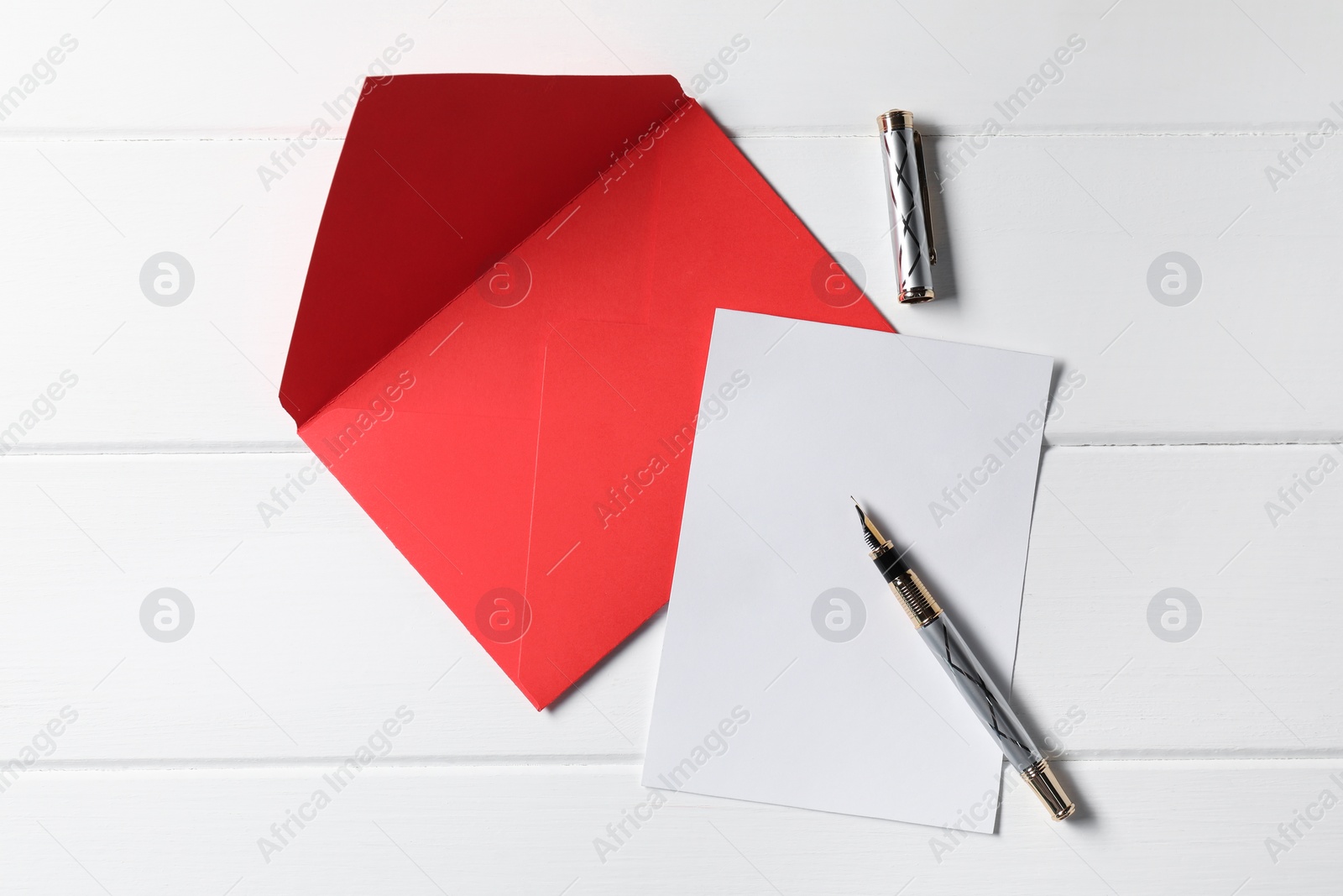 Photo of Blank sheet of paper, pen and letter envelope on white wooden table, top view. Space for text