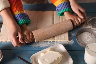 Photo of Mother and child rolling dough at blue wooden table together, closeup