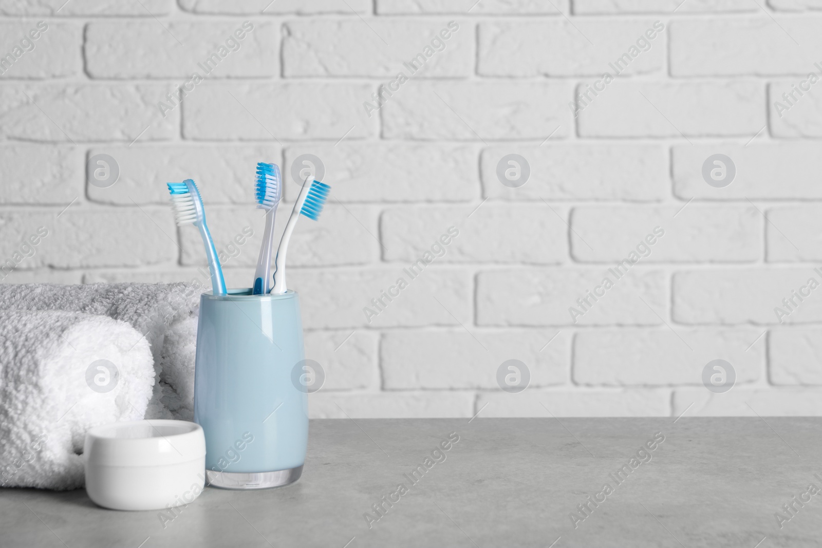Photo of Plastic toothbrushes in holder, cosmetic product and towels on light grey table. Space for text