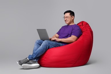 Photo of Happy man with laptop sitting in beanbag chair against grey background
