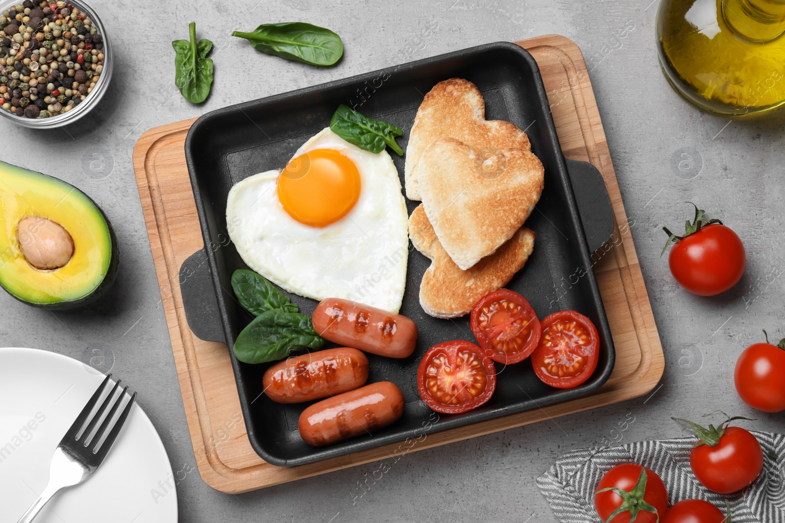 Photo of Romantic breakfast with fried sausages, heart shaped egg and toasts on grey table, flat lay. Valentine's day celebration