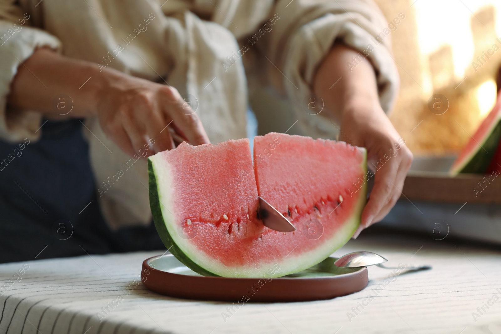 Photo of Woman cutting slice of fresh watermelon at wooden table, closeup