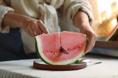 Photo of Woman cutting slice of fresh watermelon at wooden table, closeup