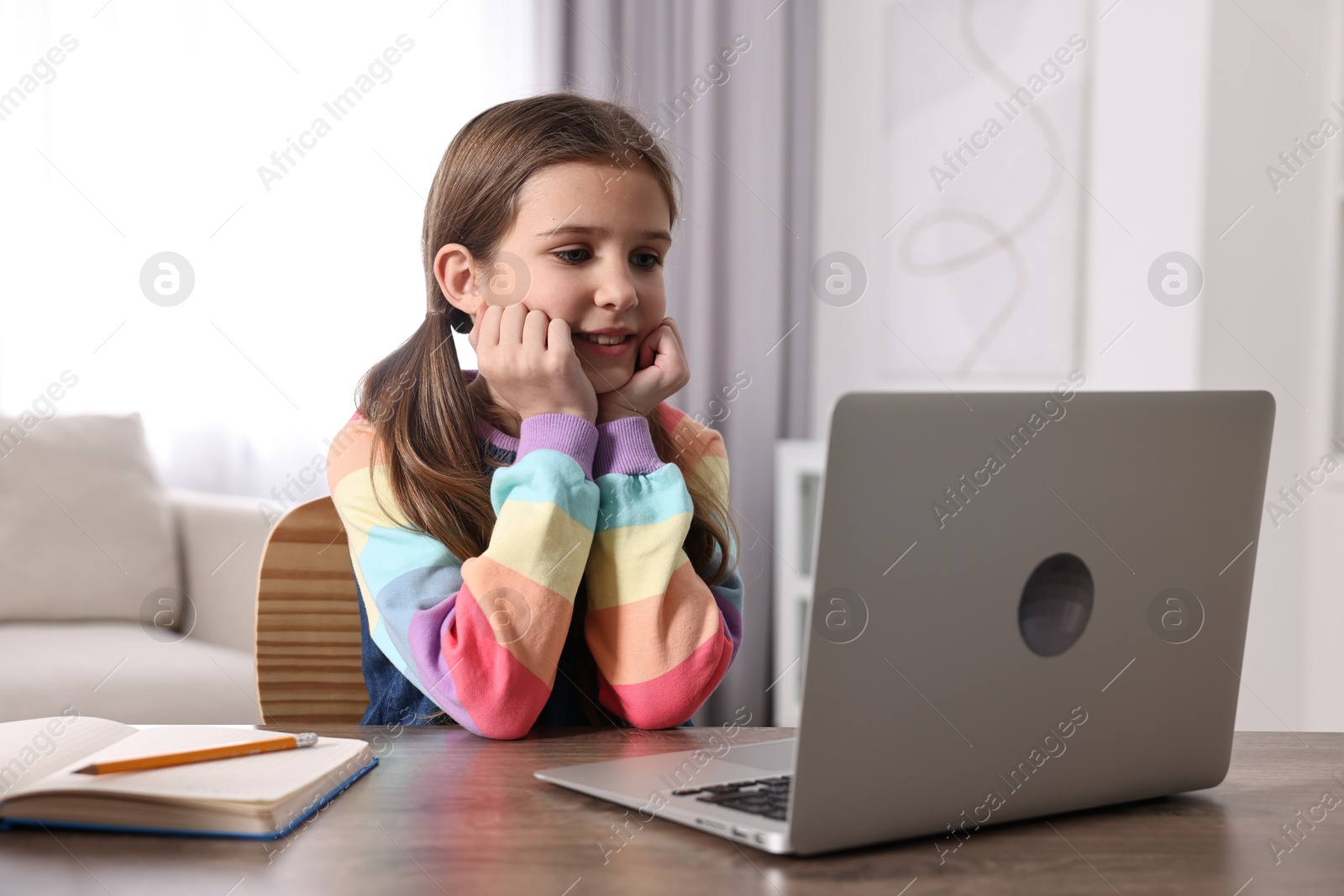 Photo of E-learning. Cute girl using laptop during online lesson at table indoors