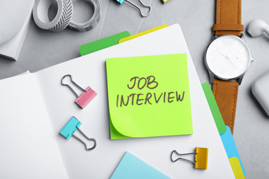 Photo of Reminder note about job interview and stationery on table, flat lay