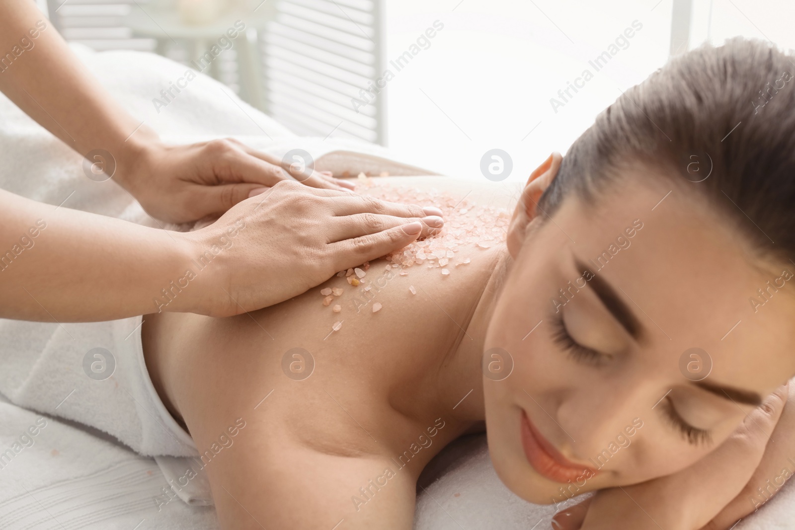 Photo of Young woman having body scrubbing procedure with sea salt in spa salon