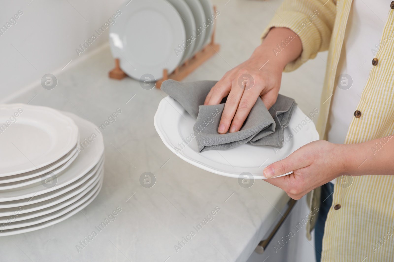 Photo of Woman wiping plate with towel at white marble table in kitchen, closeup