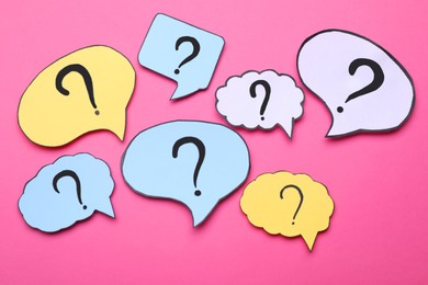 Photo of Different paper speech bubbles with question marks on pink background, flat lay