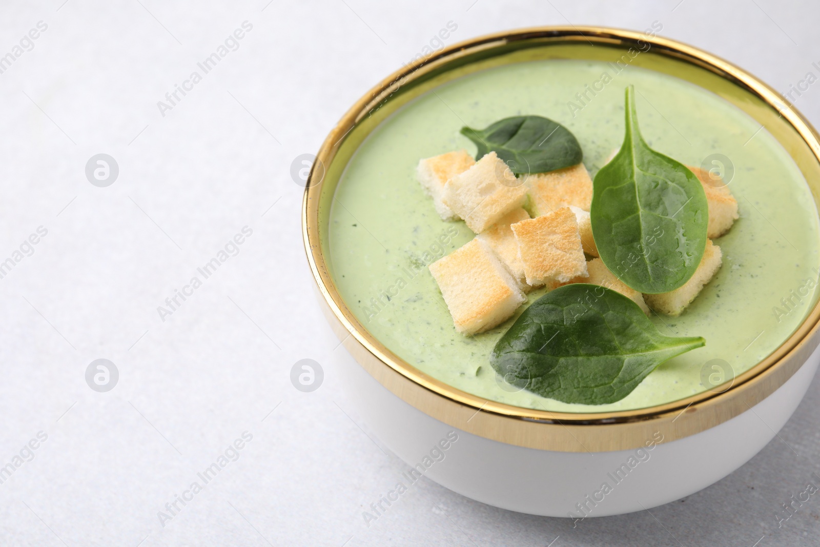 Photo of Delicious spinach cream soup with croutons in bowl on light grey table. Space for text