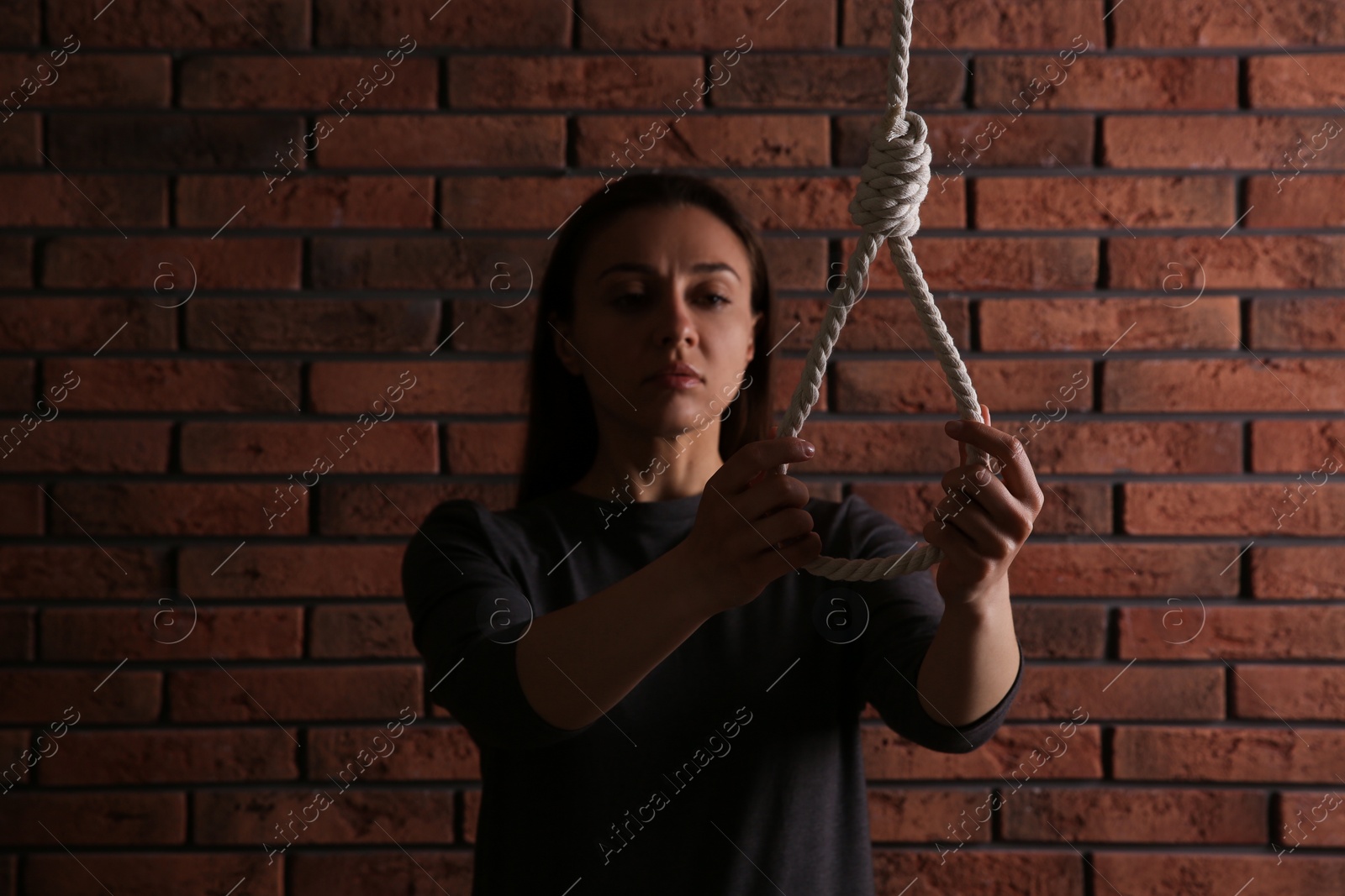 Photo of Depressed woman with rope noose near brick wall