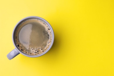 Photo of Grey mug of freshly brewed hot coffee on yellow background, top view. Space for text