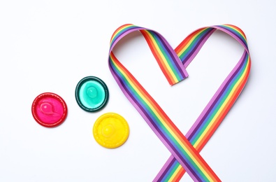 Photo of Colorful condoms and rainbow ribbon on white background, top view. LGBT concept