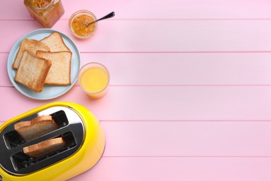 Photo of Yellow toaster with roasted bread, glass of juice and jam on pink wooden table, flat lay. Space for text
